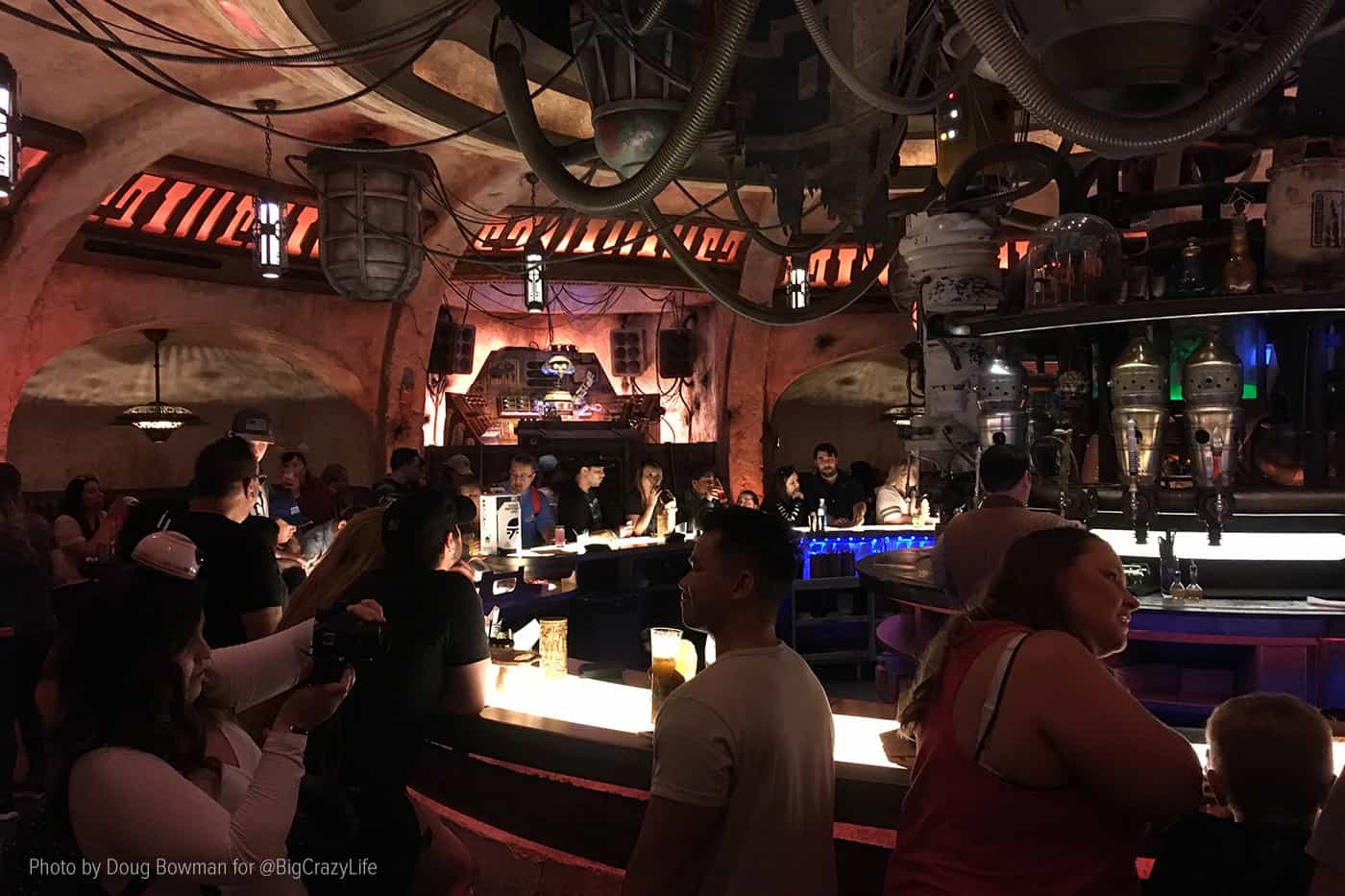 Interior shot of Oga's Cantina with the bar in the foreground and DJ R-3X spinning tunes in the background.